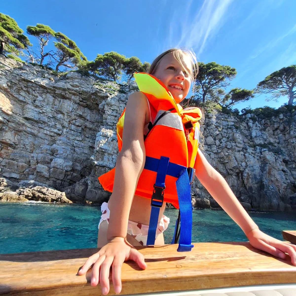 Smiling girl in a life jacket on the boat beside the island cliffs