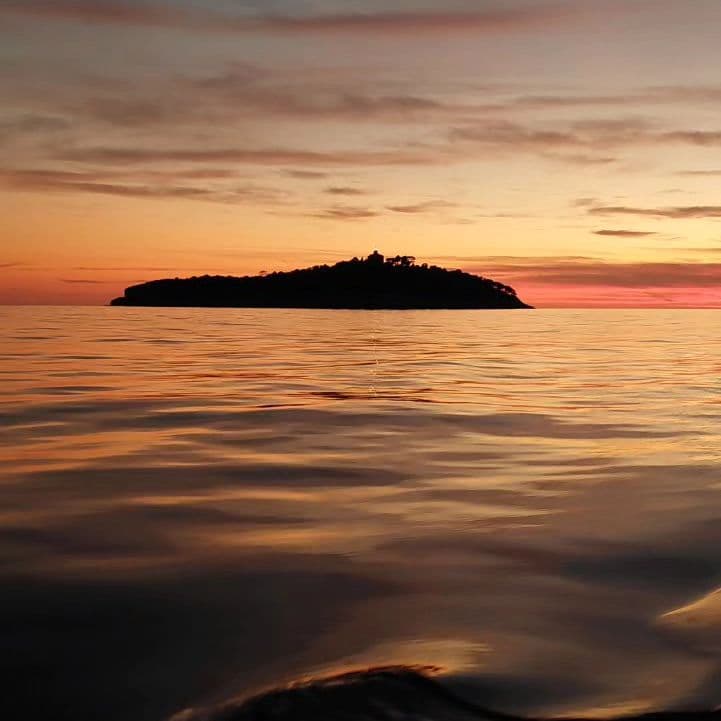 An island silhouette against an orange evening sky over calm water