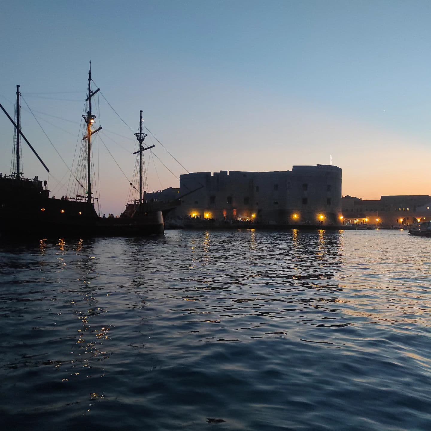 Die beleuchteten Mauern des alten Hafens und ein Segelschiff in der Dämmerung